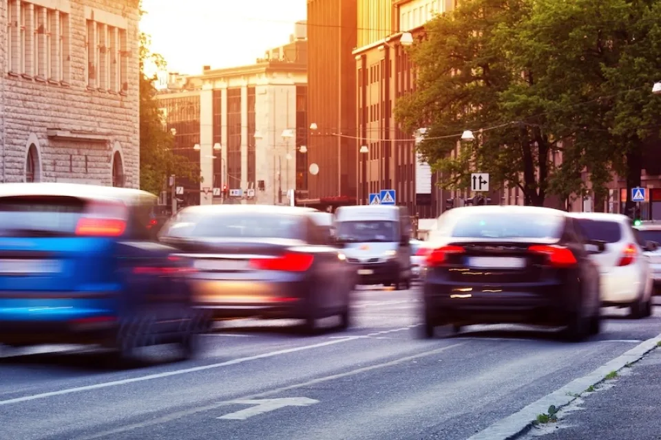 Blurred cars driving down road with European road signs visible.